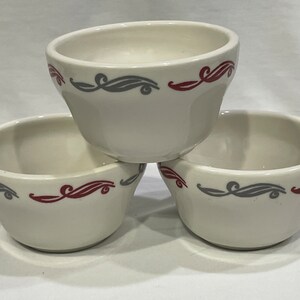 May include: Three white ceramic bowls with a gray and red swirl design. The bowls are stacked on top of each other.