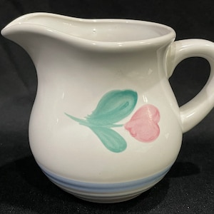 May include: White ceramic creamer with a blue and green floral design. The creamer has a rounded body and a handle.