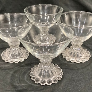 May include: Four clear glass dessert cups with a beaded base. The cups are arranged in a square shape.