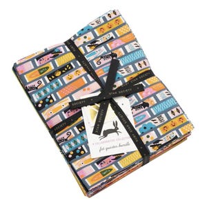 May include: A stack of folded fabric squares tied with a black ribbon featuring the text Ruby Star Society. The fabric has a repeating pattern of rectangular candy-themed graphics in orange, yellow, pink, and blue, with text like Witch's Chew.