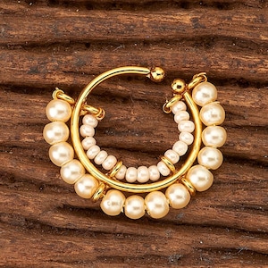 May include: A gold-coloured nose ring with a crescent design. It features two rows of white pearls and a central row of small, off-white beads. The ring has a small, round accent at the top.