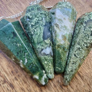 Könnte beinhalten: Vier grüne Moosachat-Pendel mit silbernen Ketten. Die Pendel sind unten spitz zulaufend und haben eine facettierte, geometrische Form.