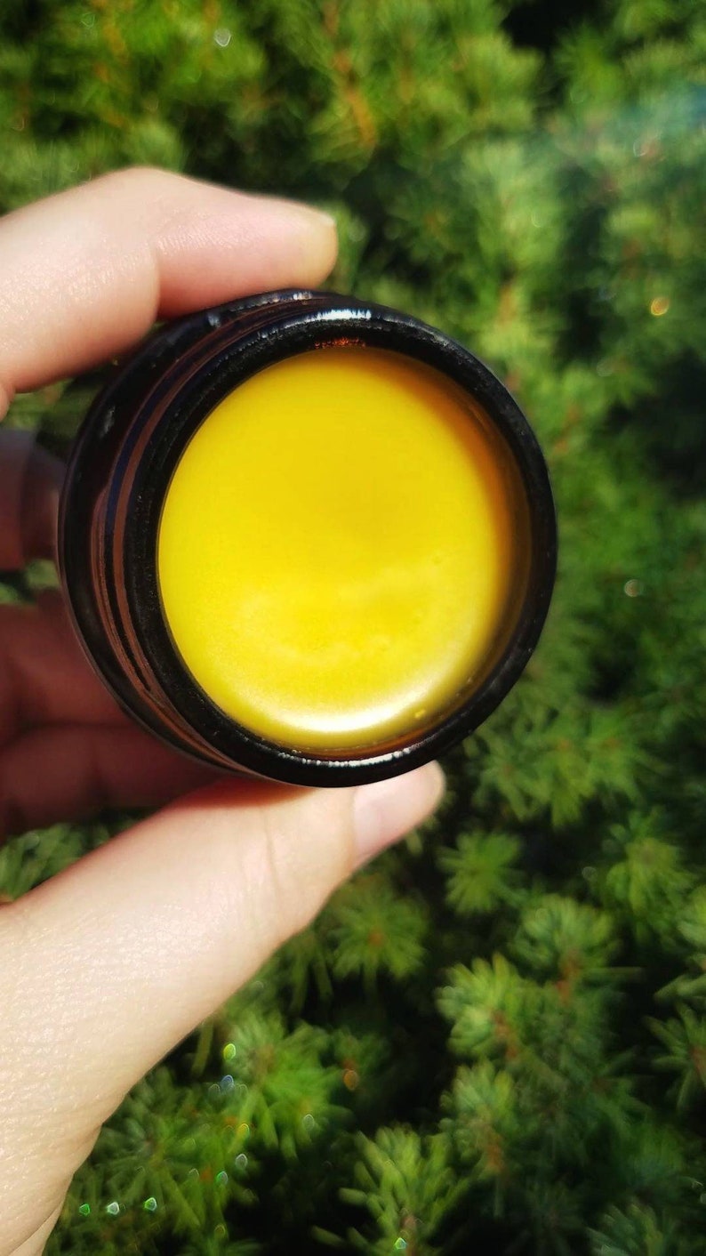 May include: A small, round jar with a black lid filled with a bright yellow balm.