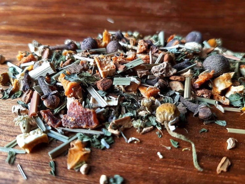 Op de afbeelding: Een close-up van een mengsel van gedroogde kruiden, specerijen en fruitschillen om thee te maken. De mix bevat gedroogde sinaasappelschil, citroenschil, kamillebloemen, citroengras, kruidnagel en andere specerijen.