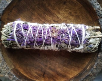 May include: A smudge stick with white string and purple dried flowers. The smudge stick is in a wooden bowl.