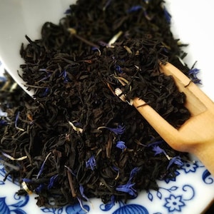 May include: A close-up of a bowl of loose leaf black tea with blue cornflower petals. The tea is in a white bowl with a blue and white floral pattern.