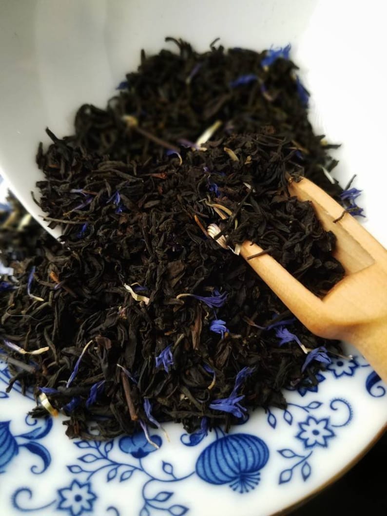 May include: A close-up of a bowl of loose leaf black tea with blue cornflower petals. The tea is in a white bowl with a blue and white floral pattern.