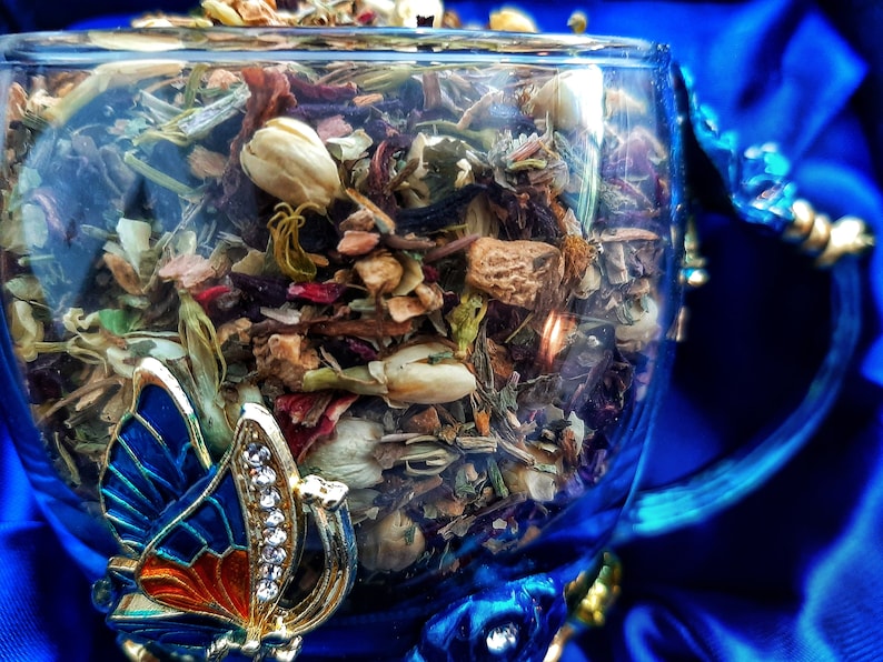 Pode incluir: Uma ch&aacute;vena de ch&aacute; de vidro com um desenho de borboleta azul na pega. A ch&aacute;vena est&aacute; cheia de uma mistura de ervas secas, flores e peda&ccedil;os de fruta.