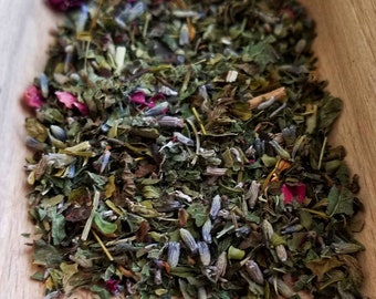 Peut inclure: Un gros plan d'une cuillère en bois remplie d'un mélange d'herbes et de fleurs séchées. Le mélange comprend des herbes vertes, des boutons de lavande et des pétales de rose roses.