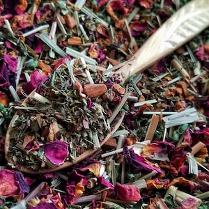 Pode incluir: Uma colher de madeira cheia de uma mistura de ervas, flores e especiarias secas. A mistura inclui ervas verdes, p&eacute;talas de rosa cor-de-rosa e paus de canela marrons.