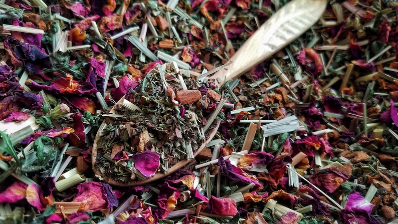 Pode incluir: Uma colher de madeira cheia de uma mistura de ervas, flores e especiarias secas. A mistura inclui ervas verdes, p&eacute;talas de rosa cor-de-rosa e paus de canela marrons.
