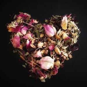 May include: A heart-shaped arrangement of dried herbs and flower petals, including rose petals, in shades of pink, white, and beige.