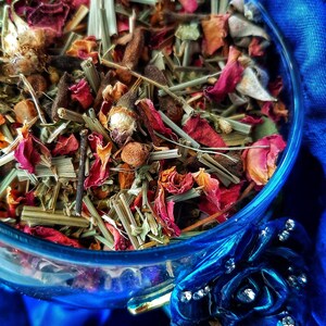 Pode incluir: Uma tigela de vidro cheia de uma mistura de ervas, flores e especiarias secas. A mistura inclui p&eacute;talas de rosa secas, capim-lim&atilde;o e outras plantas. A tigela est&aacute; sobre um fundo de tecido azul.