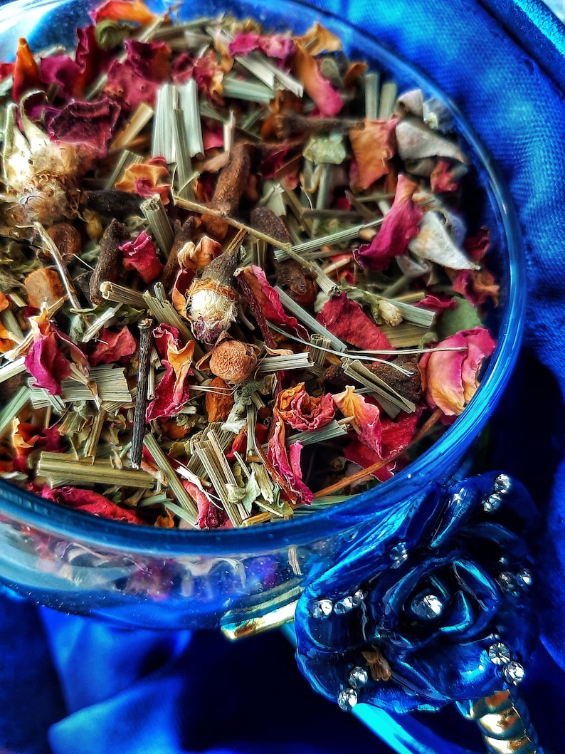 Pode incluir: Uma tigela de vidro cheia de uma mistura de ervas, flores e especiarias secas. A mistura inclui p&eacute;talas de rosa secas, capim-lim&atilde;o e outras plantas. A tigela est&aacute; sobre um fundo de tecido azul.