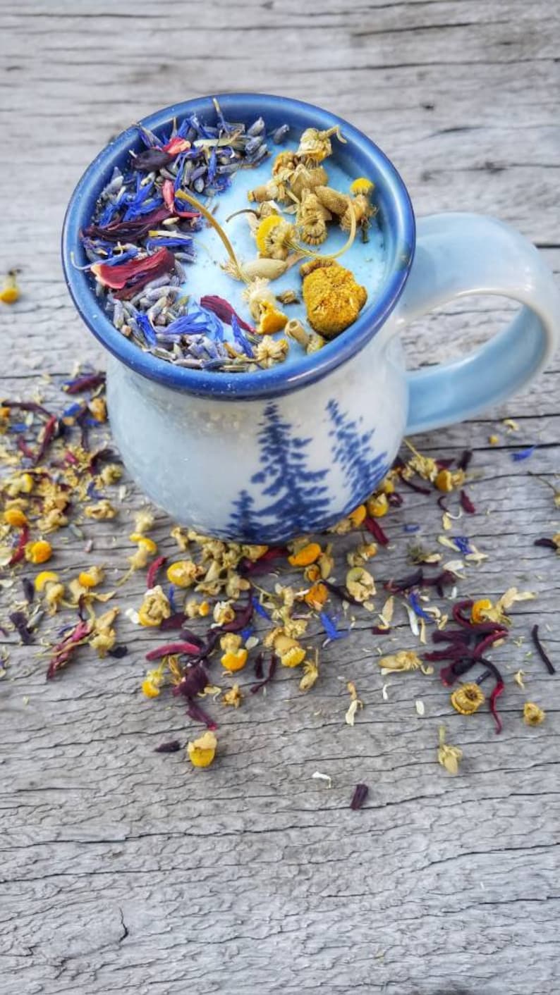 May include: A blue ceramic mug with a tree design filled with dried flowers and herbs. The mug is sitting on a wooden surface.