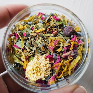 Puede incluir: Primer plano de un frasco de vidrio lleno de una mezcla colorida de hierbas y flores secas, incluyendo lavanda, pétalos de rosa y manzanilla.