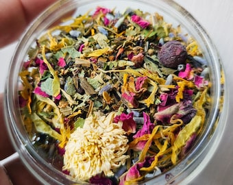 Peut inclure: Gros plan sur un bocal en verre rempli d'un mélange coloré d'herbes et de fleurs séchées, notamment de la lavande, des pétales de rose et de la camomille.