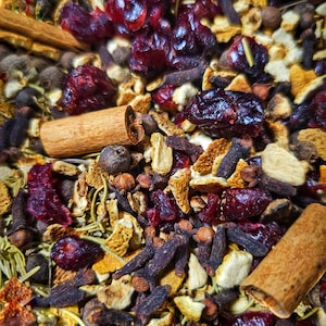 May include: A close-up of a mixture of dried fruit, spices, and citrus peels. The mixture includes cranberries, orange peel, cinnamon sticks, cloves, and allspice.