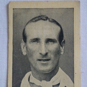 May include: Black and white photograph of a man wearing a white collared shirt and a dark suit jacket. The man is smiling and looking at the camera. The text "D. R. JARDINE" is printed below the photo.