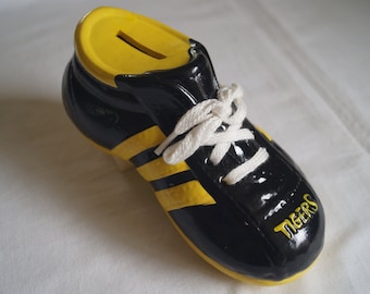 May include: Black and yellow ceramic piggy bank shaped like a football cleat with white laces. The cleat has the word "Tigers" written on the side.