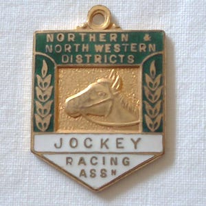May include: A gold-coloured metal pin with green and white enamel. The pin features a horse's head and the text "Northern & North Western Districts Jockey Racing Assn."
