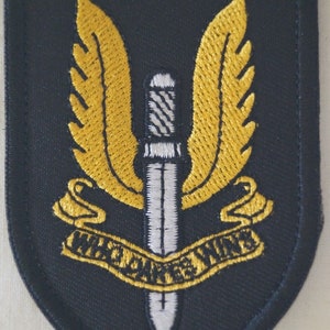 May include: A black embroidered patch with a yellow winged dagger and the text "WHO DARE WINS".
