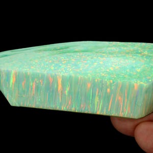 May include: A large, green opal with iridescent flashes of color. The opal is cut into a rectangular shape with rounded edges.