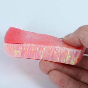 Op de afbeelding: Een roze en iriserende opaalcabochon met een glad, gepolijst oppervlak. De opaal is gezet in een roze harsbasis.
