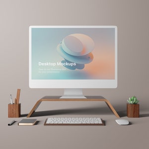 Puede incluir: Un ordenador de sobremesa blanco con un soporte de madera, un teclado, un ratón, una planta en maceta y un porta lápices con lápices y bolígrafos. La pantalla del ordenador muestra el texto "Desktop Mockups" y un diseño abstracto de colores.