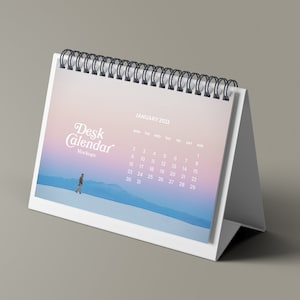 Può includere: Un mockup di calendario da tavolo bianco con un'immagine di sfondo sfumata blu e rosa. Il calendario è per gennaio 2023 e ha il testo "Desk Calendar Mockup" in alto.
