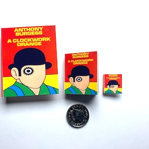 May include: Three different sized paperback books of "A Clockwork Orange" by Anthony Burgess. The covers are red, yellow, and white with a black and white illustration of a man wearing a bowler hat.
