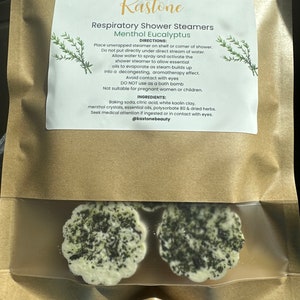 May include: Two white shower steamers with a green herbal mixture inside. The label reads "Kastone Respiratory Shower Steamers Menthol Eucalyptus" with directions and ingredients listed.