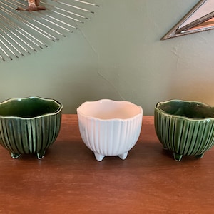 Puede incluir: Tres pequeñas macetas de cerámica con un diseño acanalado. Dos son verdes y una es blanca. Las tres tienen tres pequeños pies.