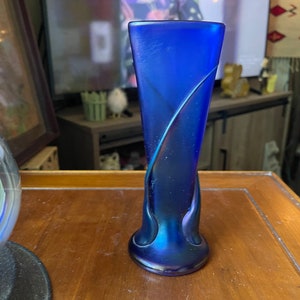 Può includere: Un vaso di vetro blu iridescente con un design a spirale unico. Il vaso è alto e sottile con una base arrotondata.