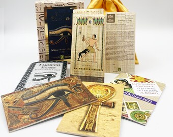 May include: A set of tarot cards with a gold and black design. The cards feature images of the Egyptian Eye of Horus, an ankh, and a dog. The cards are part of a larger set of tarot cards called "The Egyptian Tarot".