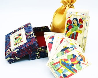 May include: A vintage tarot card deck, presented with a box and a gold satin drawstring bag. The box has a blue and red marbled design with a central illustration. The cards feature colorful illustrations of figures and symbols.