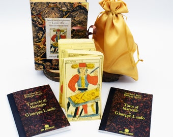 May include: A deck of Lando 1832 Marseille-Piedmont tarot cards featuring the Le Bateleur card in front, a marbled storage box, a gold satin drawstring pouch, and two companion booklets titled Tarocchi di Marsiglia and Tarot of Marseille.