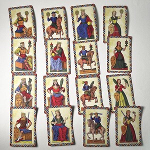 May include: A set of vintage tarot cards with illustrations of royalty and figures in historical dress. Each card has a decorative border and depicts a king, queen, or other character holding various objects. The cards are arranged on a white surface.