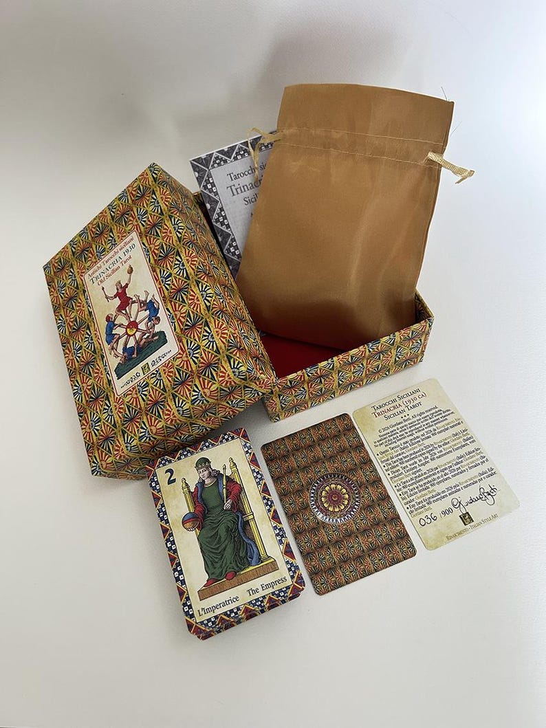 May include: A tarot card set featuring a patterned box, a brown drawstring bag, and several cards. One card displays "L'imperatrice The Empress". The box is labelled "TRINACRIA 1930".