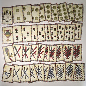 May include: A set of vintage playing cards with illustrations of coins, cups, swords, and clubs. The cards have a cream background with decorative borders and various symbols. The deck includes an eagle emblem and a vase illustration.