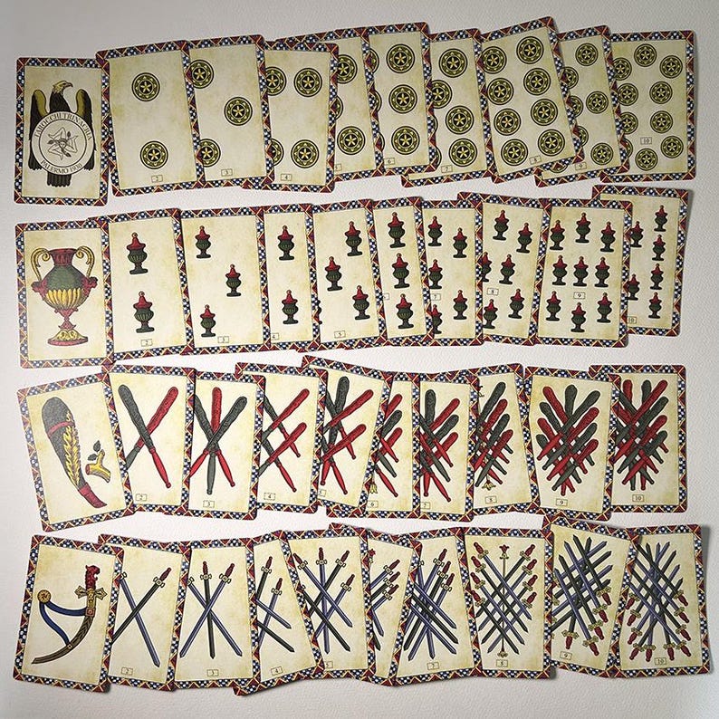 May include: A set of vintage playing cards with illustrations of coins, cups, swords, and clubs. The cards have a cream background with decorative borders and various symbols. The deck includes an eagle emblem and a vase illustration.