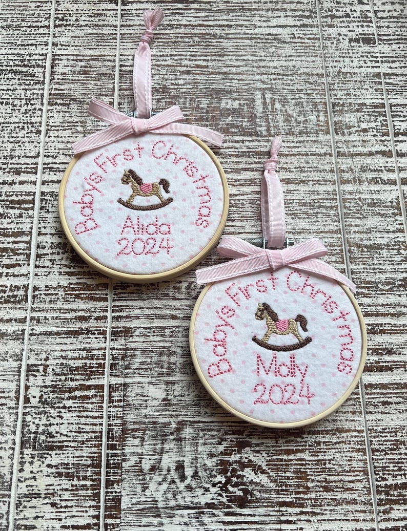 Pode incluir: Dois enfeites de Natal personalizados para o primeiro Natal de um beb&ecirc;, de cor rosa e branca, com um design de cavalo de balan&ccedil;o. Os enfeites s&atilde;o bordados com os nomes "Aida" e "Molly" e o ano "2024".