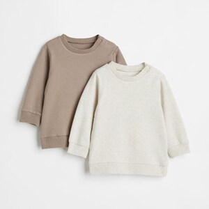 May include: Two long-sleeved sweatshirts, one brown and one light gray, are laid out on a white background.