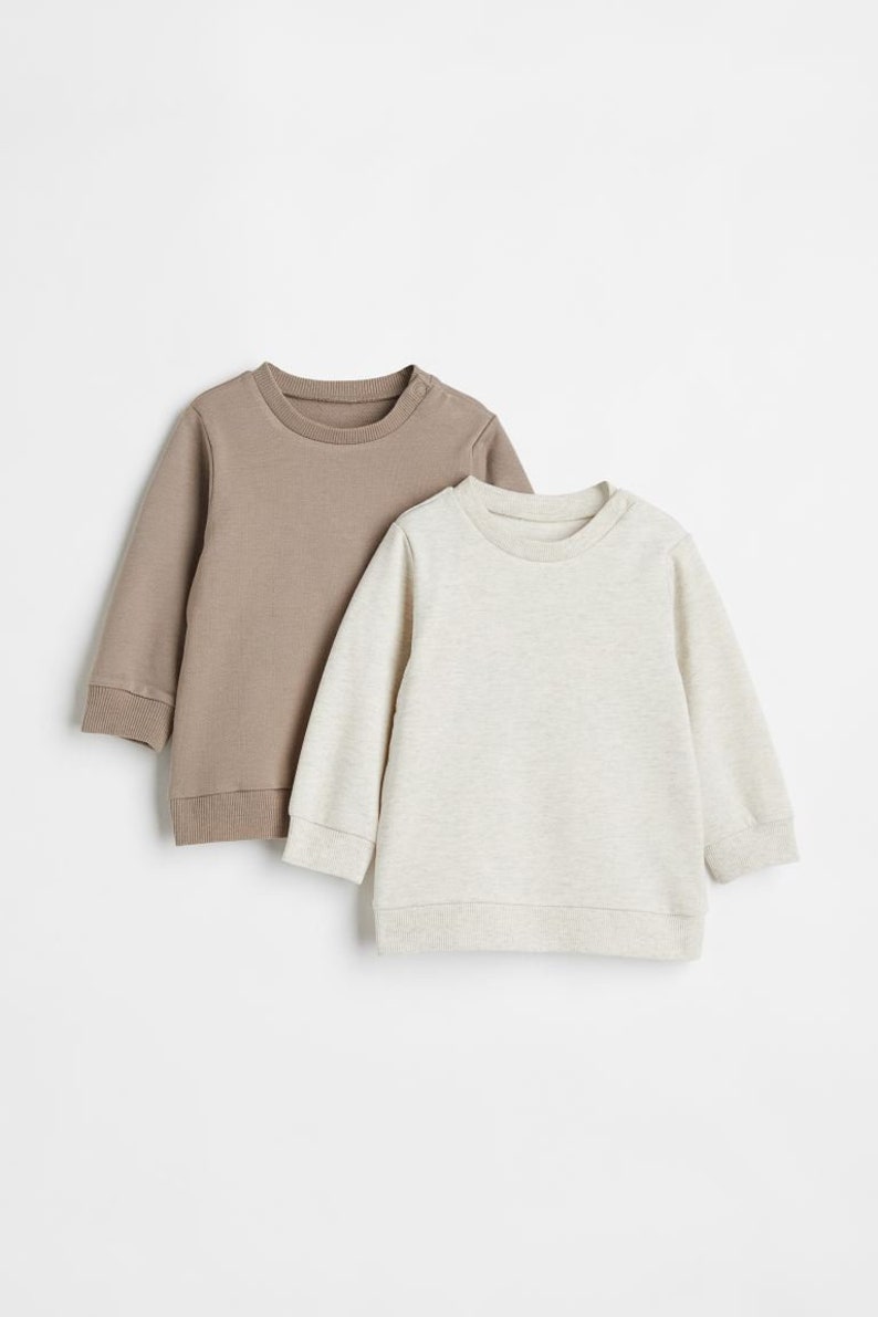 May include: Two long-sleeved sweatshirts, one brown and one light gray, are laid out on a white background.