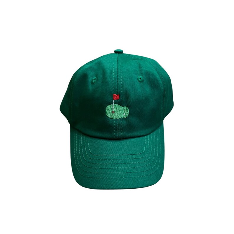 Op de afbeelding: Een groene baseballpet met een geborduurd groen golfveld en een rode vlag aan de voorkant.