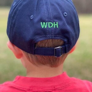 May include: A navy blue baseball cap with an adjustable strap at the back. The cap has green embroidery that reads "WDH".