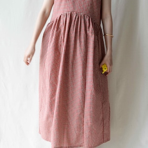May include: A red and white gingham sleeveless dress with a v-neckline. The dress has a gathered waist and falls to the ankles.