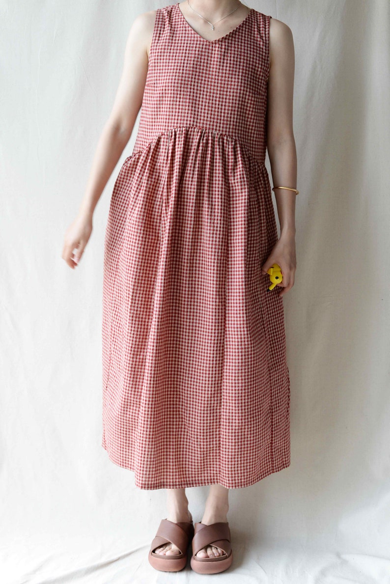 May include: A red and white gingham sleeveless dress with a v-neckline. The dress has a gathered waist and falls to the ankles.