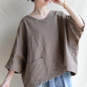 May include: A brown and beige gingham shirt with a v-neck and a patch pocket. The shirt has a relaxed fit and 3/4 sleeves.