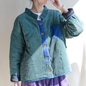 Puede incluir: Una chaqueta de pana verde con un panel y un bolsillo de mezclilla azul. La chaqueta tiene un cuello alto y cierre de botón.